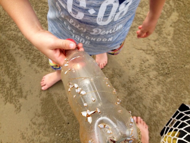 Picking up a plastic bottle at the beach to put in the bin.