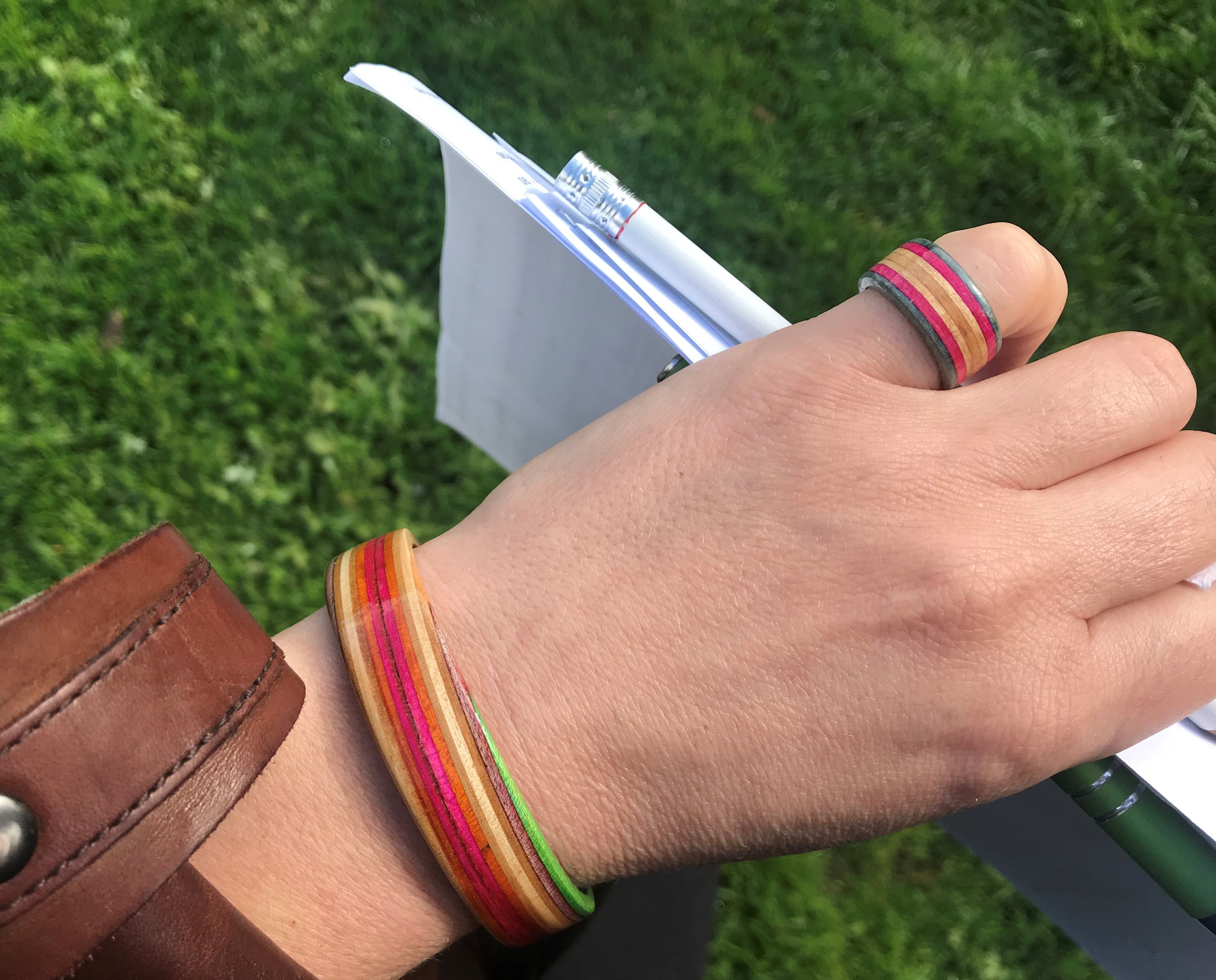 A bangle and ring made from upcycled broken skateboards shown on a female hand.